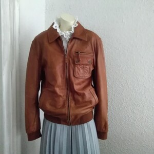 May include: A brown leather bomber jacket with a zipper closure and a large pocket on the left side.