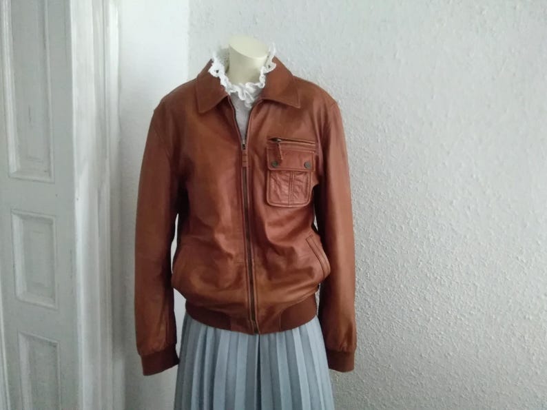 May include: A brown leather bomber jacket with a zipper closure and a large pocket on the left side.