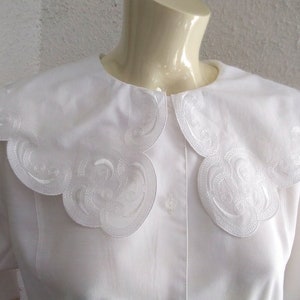 Puede incluir: Blusa blanca con un cuello grande festoneado con un dise&ntilde;o bordado. El cuello est&aacute; hecho de una tela blanca delicada y tiene un borde ligeramente fruncido.