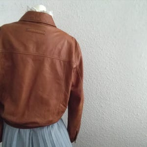 May include: A brown leather jacket with a button-up collar and a small label on the back that says "Genuine Leather".