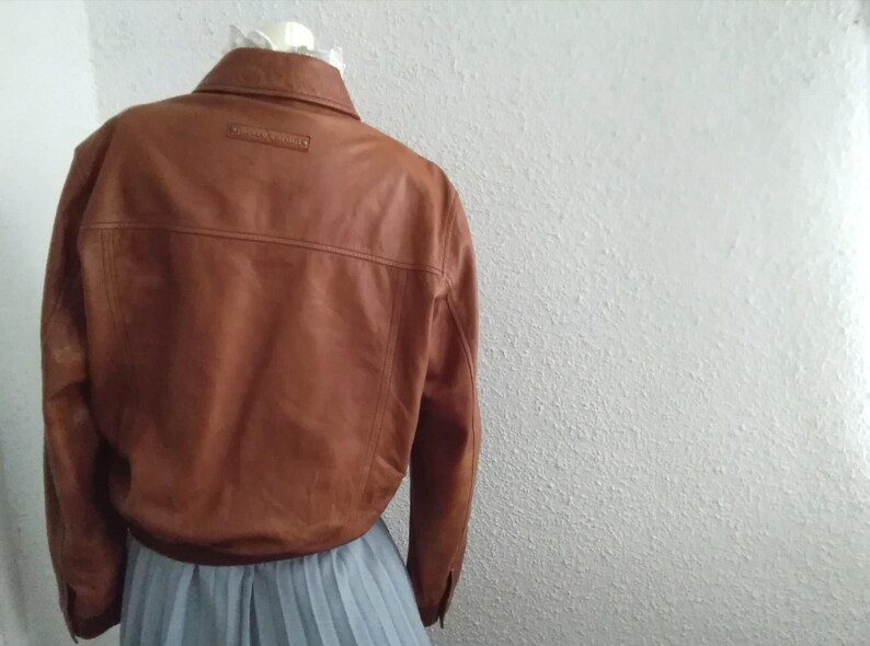 May include: A brown leather jacket with a button-up collar and a small label on the back that says "Genuine Leather".
