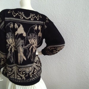 May include: Black knitted sweater with a beige pattern of birds and geometric designs.