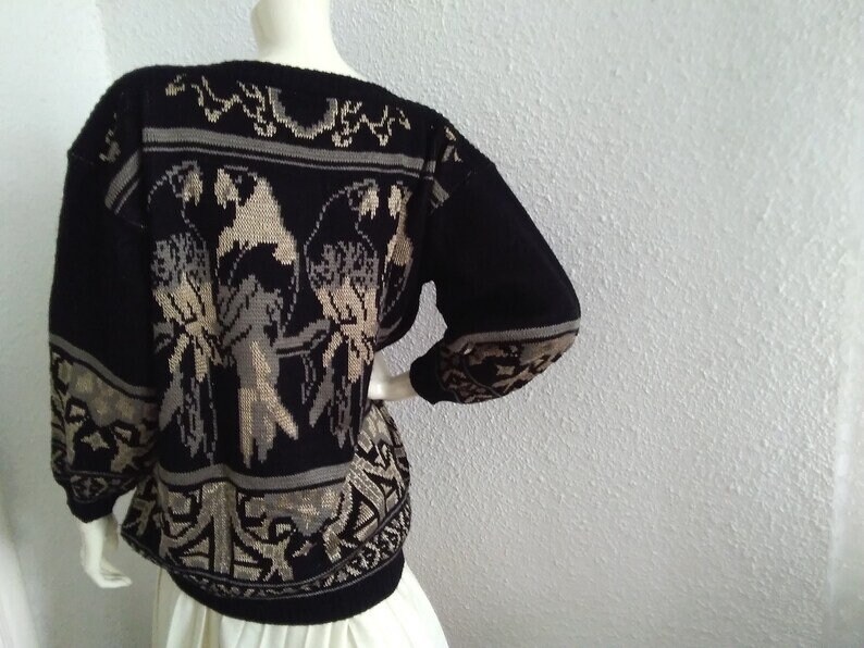 May include: Black knitted sweater with a beige pattern of birds and geometric designs.