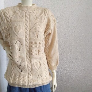 May include: A cream knitted jumper with a cable knit design and various textured patterns, including hearts, leaves, and bobbles.
