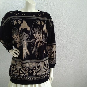 May include: Black and beige knitted jumper with a parrot design. The jumper has a crew neck and long sleeves.