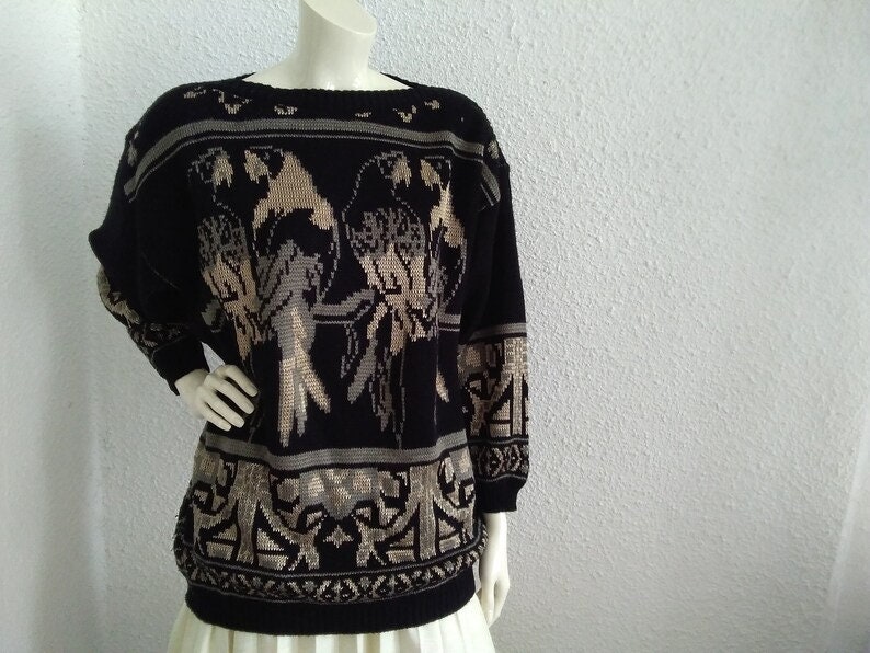 May include: Black and beige knitted jumper with a parrot design. The jumper has a crew neck and long sleeves.
