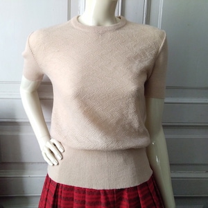 May include: A beige short-sleeved sweater with a delicate diamond pattern. The sweater has a ribbed hem and is made of a soft, lightweight material.