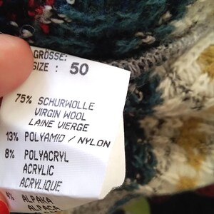 May include: A white tag with black text detailing the composition of a sweater. The tag states "GR&Ouml;SSE: SIZE: 50" and lists the percentages of Schurwolle (Virgin Wool), Polyamid (Nylon), Polyacryl (Acrylic), and Alpaka (Alpaca).