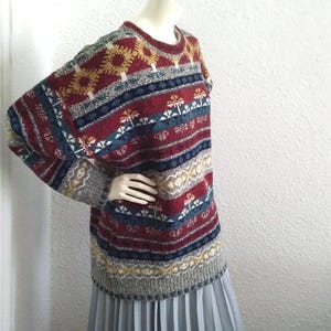 May include: A colorful, striped sweater with a geometric pattern in shades of red, blue, yellow, and white. The sweater has a crew neck and long sleeves.