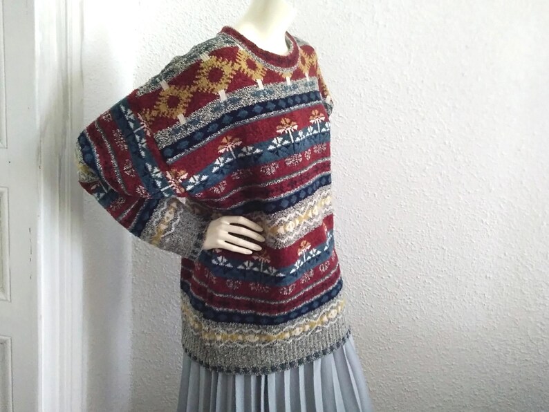 May include: A colorful, striped sweater with a geometric pattern in shades of red, blue, yellow, and white. The sweater has a crew neck and long sleeves.