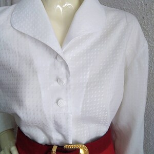 May include: White button-down blouse with a textured pattern and a wide collar. The blouse is worn with a red skirt and a gold belt.