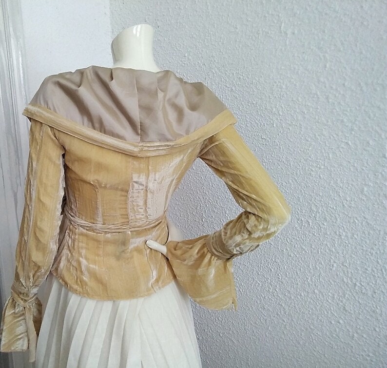 May include: A gold velvet jacket with a wide, off-the-shoulder collar and long sleeves. The jacket has a fitted waist and a slightly flared hem. The sleeves have a gathered detail at the cuffs.