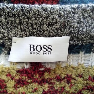 May include: A close-up of a white label with black text that reads "BOSS HUGO BOSS" on a gray and white knit sweater with a colorful pattern.