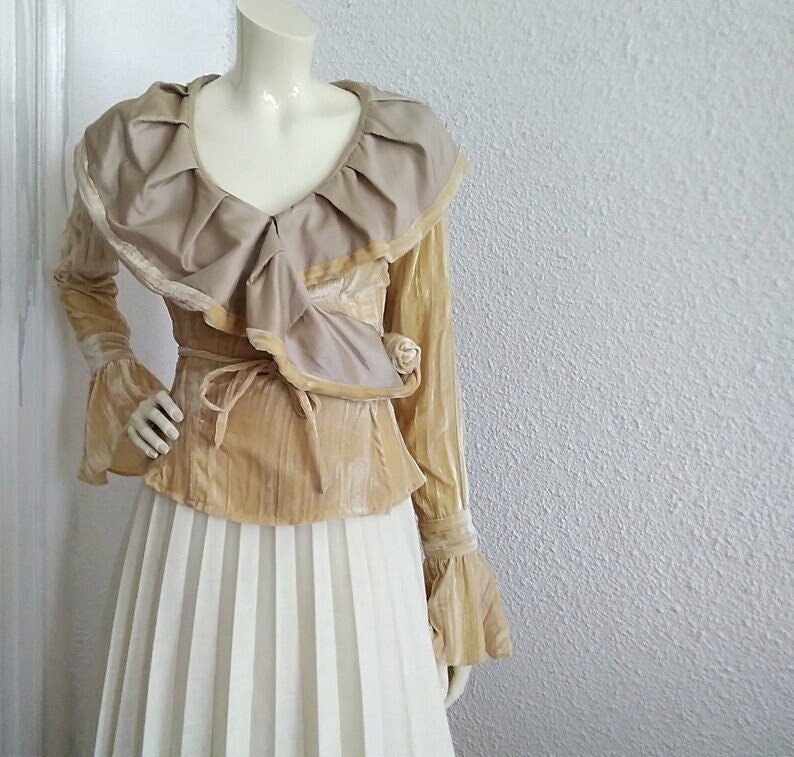 May include: A gold velvet blouse with a large ruffled collar and long sleeves. The blouse has a tie at the waist and a delicate floral pattern.