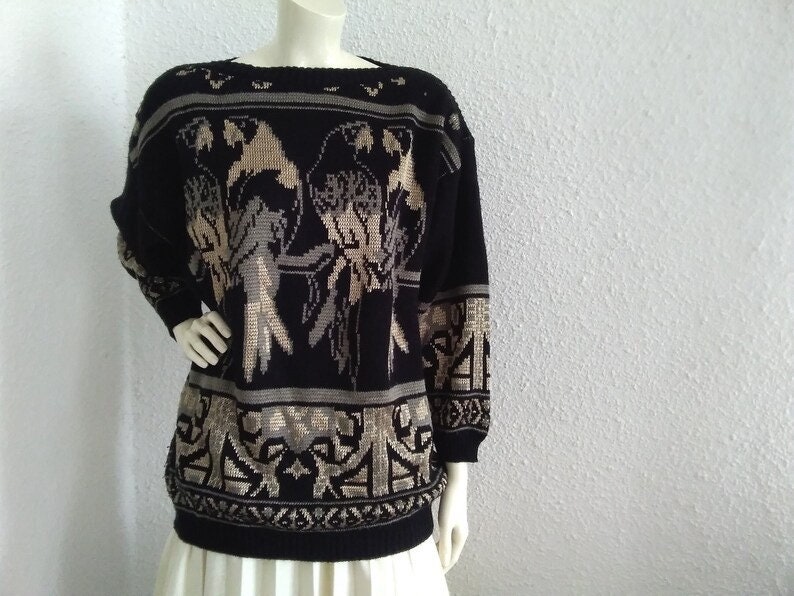May include: Black knitted jumper with a beige and grey parrot design. The jumper has a wide, round neckline and long sleeves.