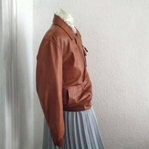 May include: A brown leather bomber jacket with a zipper closure and a gray pleated skirt.