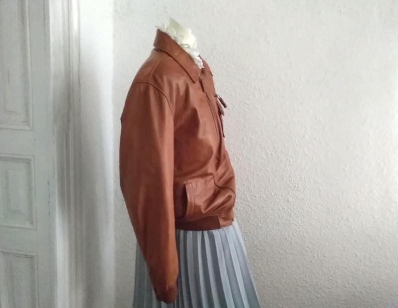 May include: A brown leather bomber jacket with a zipper closure and a gray pleated skirt.