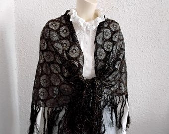 May include: A black lace shawl with a floral pattern and fringe, draped over a white blouse with a ruffled collar. The shawl is made of a delicate, open-weave fabric, and the overall style is vintage.