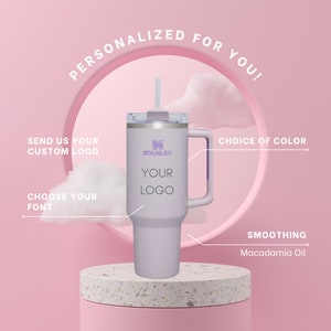 May include: A personalized stainless steel travel mug with a purple lid and handle. The mug has a white background with the text "STANLEY" and "YOUR LOGO" in black. The mug is sitting on a pink and white surface. The text "PERSONALIZED FOR YOU!" is in a circle above the mug. The text "SEND US YOUR CUSTOM LOGO" is on the left side of the mug. The text "CHOOSE YOUR FONT" is below the mug. The text "CHOICE OF COLOR" is on the right side of the mug. The text "SMOOTHING Macadamia Oil" is below the mug.