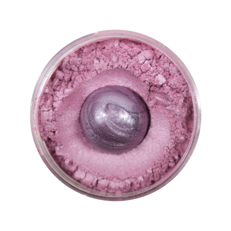 Pu&ograve; includere: Un piccolo contenitore rotondo di pigmento cosmetico rosa in polvere con una sfera metallica viola al centro.