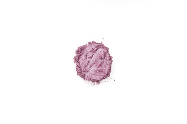 Pu&ograve; includere: Un piccolo campione di polvere di ombretto viola sciolta su uno sfondo bianco.