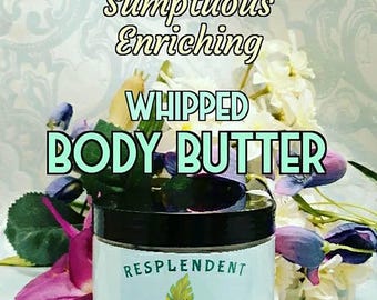 Puede incluir: Un tarro azul y blanco de mantequilla corporal batida etiquetado como "Resplendent Earth Tone Essences Whipped Body Butter 237 ml". El tarro está rodeado de flores blancas y moradas.