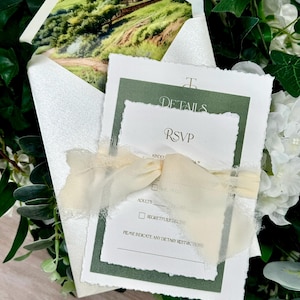 May include: Wedding invitation set with a landscape scene inside the envelope. The invitation suite includes a details card, RSVP card, and a cream-coloured ribbon. The text on the cards includes "DETAILS" and "RSVP".