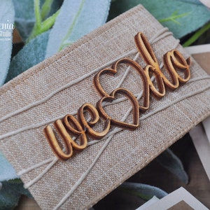 K&ouml;nnte beinhalten: Nahaufnahme einer rustikalen Burlap-Hochzeitsgeschenkbox mit dem Wort "Hochzeit" in Kursivschrift auf einem Holzhertz. Die Box ist mit Schnur gebunden und hat ein nat&uuml;rliches, erdiges Gef&uuml;hl.