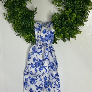 May include: A white and blue floral ribbon tied around a green wreath. The ribbon has a blue and white floral pattern.