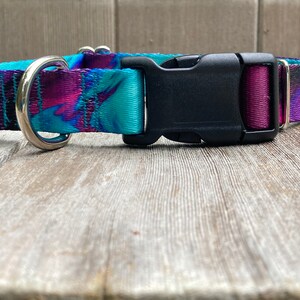 May include: A purple, blue, and black patterned dog collar with a silver D-ring and a black plastic buckle.