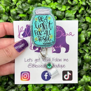 The badge reel features a mason jar charm with a turquoise blue glitter background. Inside the jar are the words "BE A light FOR ALL TO SEE" and "Matthew 5:16."