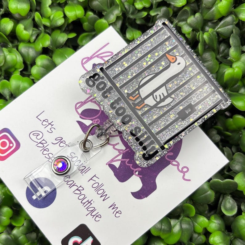 The badge reel features a cartoon white goose behind black prison bars, with the text "got too silly" in white letters on a black background below the bars. The badge reel has a clear plastic retractable cord and a snap closure, with a small, iridescent gemstone attached near the bottom.