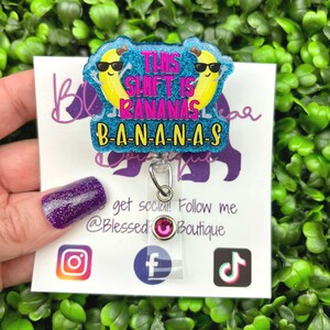 May include: A badge reel with a glittery blue background and the text "THIS SHIFT IS BANANAS B-A-N-A-N-A-S". The badge reel features two yellow bananas wearing sunglasses. The badge reel has a clear plastic holder and a silver clip.