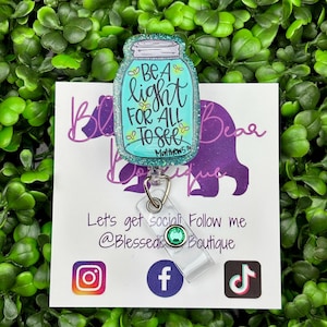 The badge reel features a mason jar charm with a turquoise blue glitter background. Inside the jar are the words "BE A light FOR ALL TO SEE" and "Matthew 5:16."