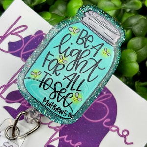 The badge reel features a mason jar charm with a turquoise blue glitter background. Inside the jar are the words "BE A light FOR ALL TO SEE" and "Matthew 5:16."