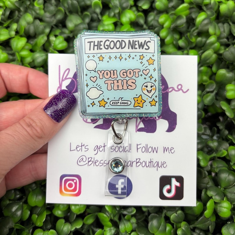 May include: A light blue badge reel with the text "THE GOOD NEWS YOU GOT THIS KEEP GOING." The badge reel has a glittery border and features cartoon graphics of stars, clouds, and a smiling face. A clear plastic reel with a silver clip is attached.