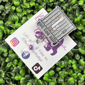 The badge reel features a cartoon white goose behind black prison bars, with the text "got too silly" in white letters on a black background below the bars. The badge reel has a clear plastic retractable cord and a snap closure, with a small, iridescent gemstone attached near the bottom.
