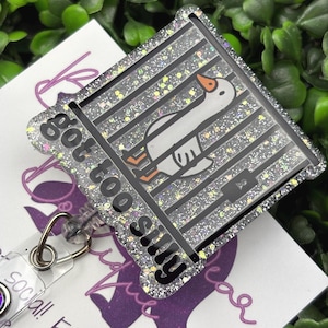 The badge reel features a cartoon white goose behind black prison bars, with the text "got too silly" in white letters on a black background below the bars. The badge reel has a clear plastic retractable cord and a snap closure, with a small, iridescent gemstone attached near the bottom.