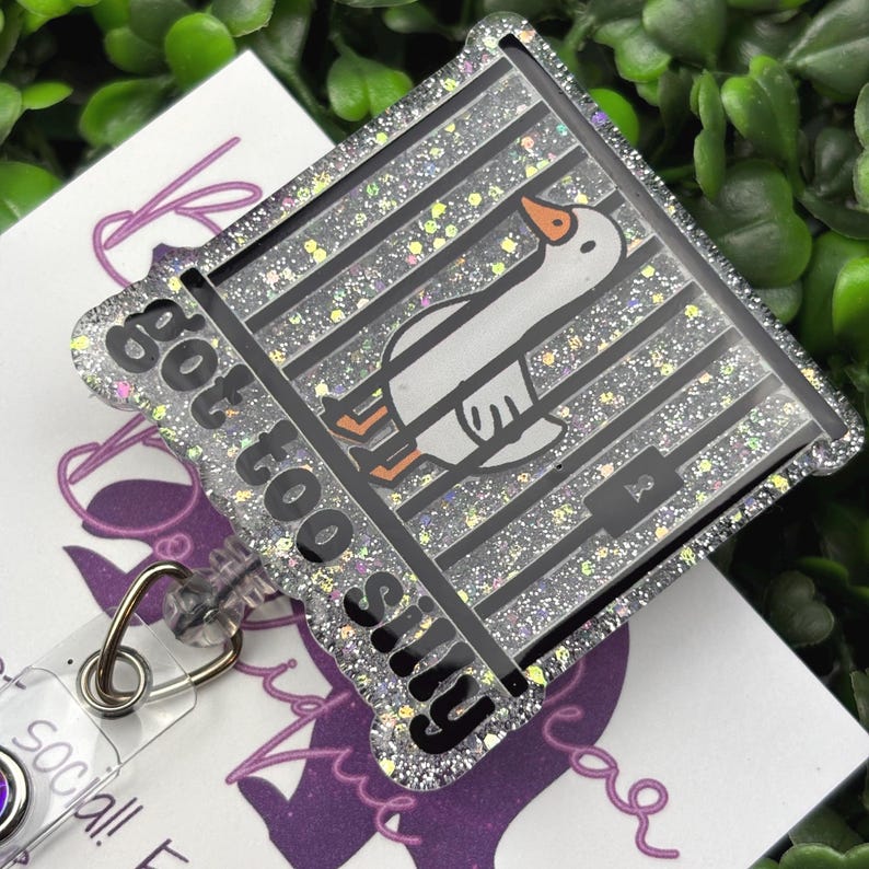 The badge reel features a cartoon white goose behind black prison bars, with the text "got too silly" in white letters on a black background below the bars. The badge reel has a clear plastic retractable cord and a snap closure, with a small, iridescent gemstone attached near the bottom.