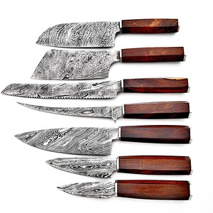 Può includere: Set di sette coltelli da cucina con lame a motivi e manici in legno scuro. I coltelli sono disposti in una pila verticale, con il coltello più grande in cima e il coltello più piccolo in fondo.