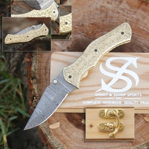May include: A gold pocket knife with a floral pattern on the handle and a Damascus steel blade. The knife is in a wooden box with a brass latch.