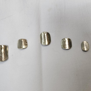 May include: Five silver-toned, rectangular-shaped metal objects are arranged on a white surface. Each object has a slightly textured surface and rounded edges. The sizes vary, with the largest on the left and the smallest on the right.