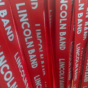 Op de afbeelding: Een stapel rode stoffen lanyards met witte tekst die "Lincoln Band" zegt.
