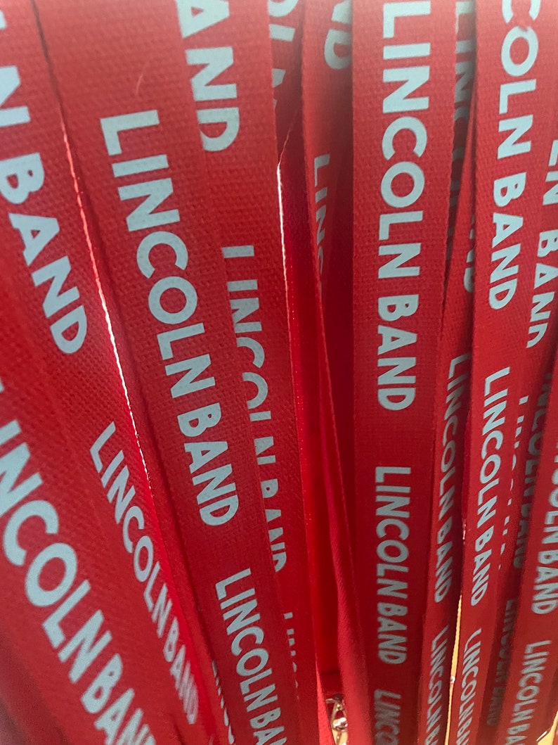 Op de afbeelding: Een stapel rode stoffen lanyards met witte tekst die "Lincoln Band" zegt.