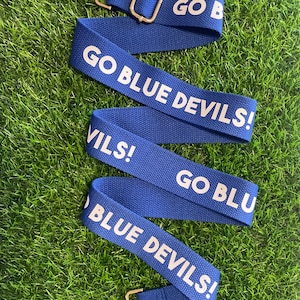 Op de afbeelding: Blauw-witte verstelbare band met de tekst "GO BLUE DEVILS!" aan beide kanten.
