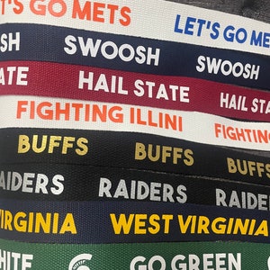 Op de afbeelding: Een close-up van een stapel kleurrijke stoffen polsbandjes met verschillende college-teamlogo's en slogans, waaronder "Let's Go Mets", "Swoosh", "Hail State", "Fighting Illini", "Buffs", "Raiders", "West Virginia" en "Go Green".