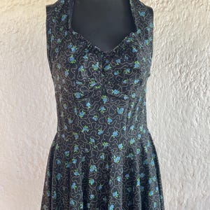 May include: A black halter dress with a floral pattern of small blue roses and white dotted lines. The dress has a fitted bodice and a flared skirt, displayed on a black mannequin.