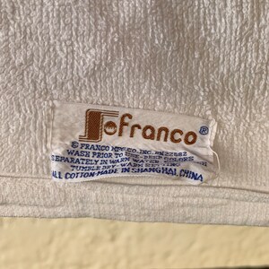 Puede incluir: Una toalla blanca con una etiqueta marr&oacute;n y azul que dice "Jofranco" e incluye instrucciones de lavado. La etiqueta dice "Franco Mfg. Co. Inc. RN22582 Lavar antes de usar - colores oscuros por separado en agua tibia - ciclo suave - secar en secadora - ajuste c&aacute;lido Todo algod&oacute;n - hecho en Shanghai, China"