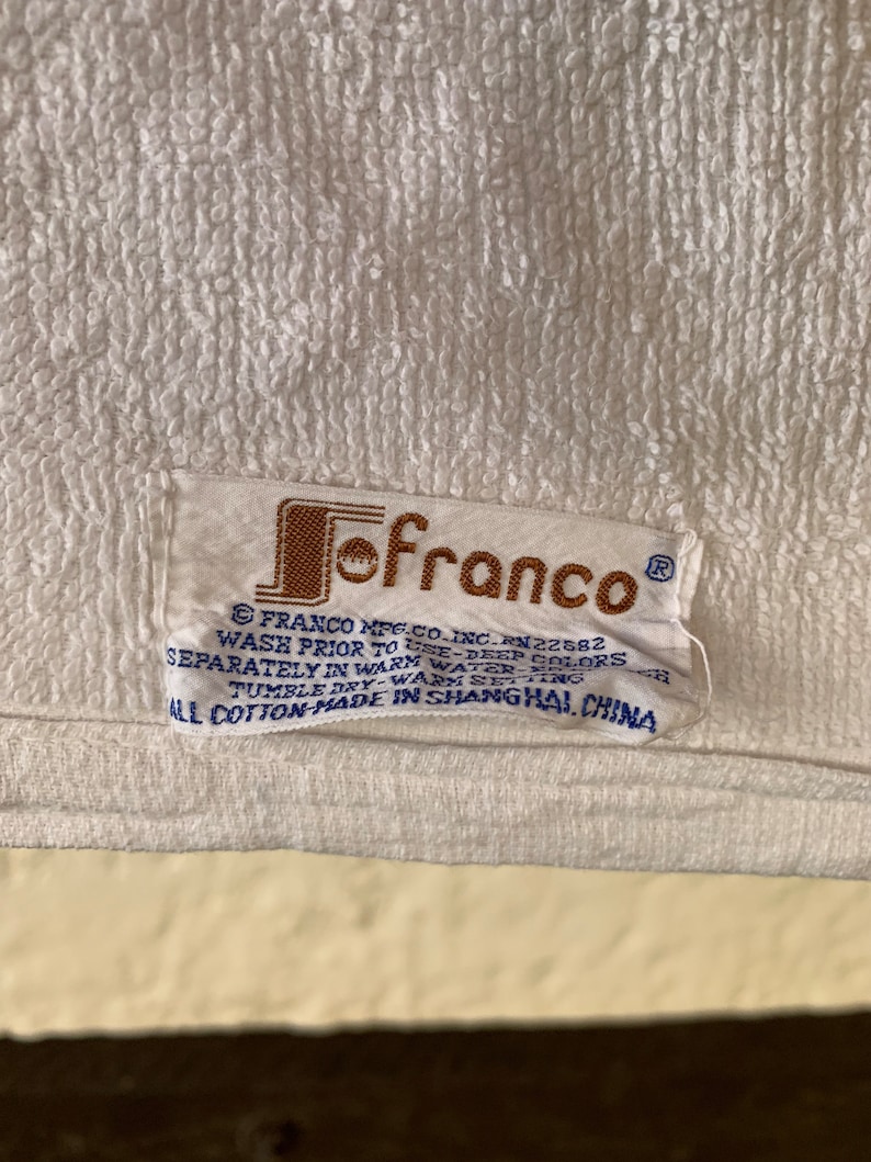 Puede incluir: Una toalla blanca con una etiqueta marr&oacute;n y azul que dice "Jofranco" e incluye instrucciones de lavado. La etiqueta dice "Franco Mfg. Co. Inc. RN22582 Lavar antes de usar - colores oscuros por separado en agua tibia - ciclo suave - secar en secadora - ajuste c&aacute;lido Todo algod&oacute;n - hecho en Shanghai, China"