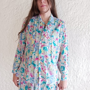 May include: A long-sleeved button-up shirt and matching pants in a white base with a colorful abstract print. The print features shades of pink, blue, yellow, and orange.
